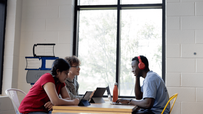 three students sitting at a desk, prepping for class